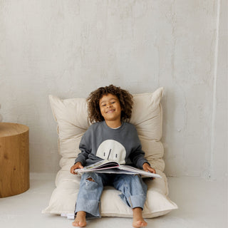 Child sitting on a tufted mattress reading a book in a cozy room.