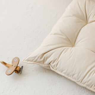 Beige canvas floor pillow on a textured white surface with a wooden hook.