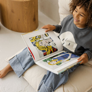 Child sitting on a floor pillow reading a colorful book