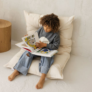 Child reading a book on a French style cushioned pillow in a cozy room.
