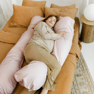 Pregnant woman lying comfortably with the MINICAMP shell pink U-shaped maternity pillow.