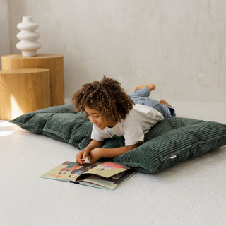 Child reading a book on a French Style green cushion in a minimalistic room.