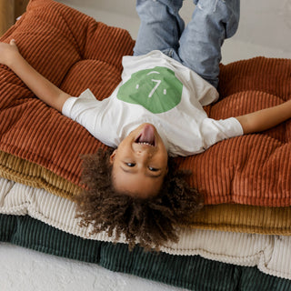 Child lying on a tufted corduroy mattresses with a white shirt 